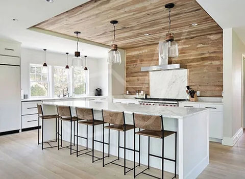 Cocina blanca con isla, taburetes altos y techo revestido de madera